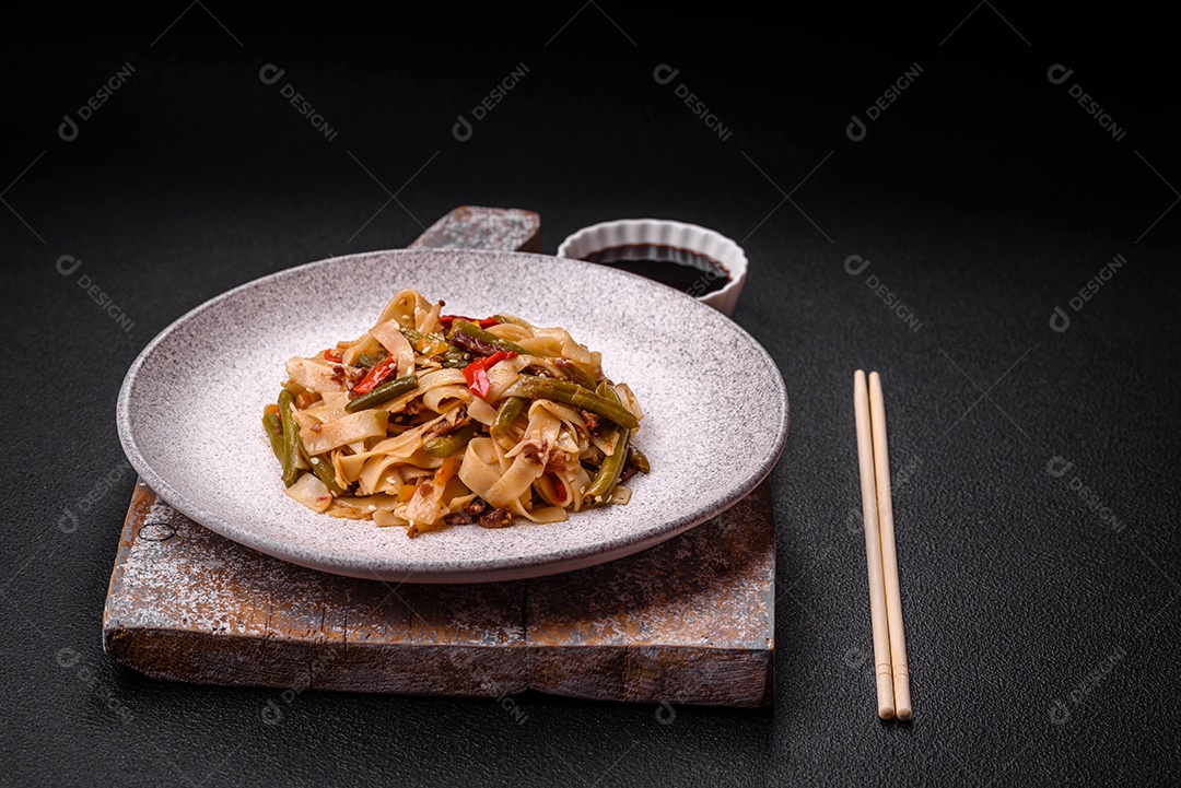 Delicioso prato asiático udon com pimenta, feijão verde, especiarias e ervas em uma placa cerâmica sobre um fundo escuro de concreto