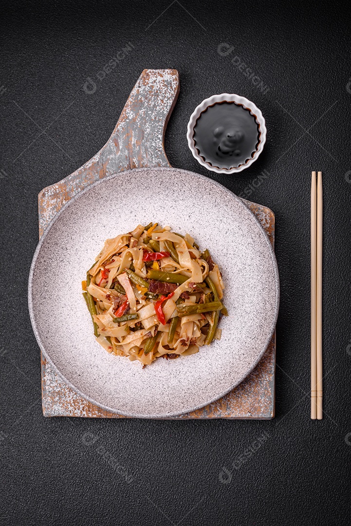 Delicioso prato asiático udon com pimenta, feijão verde, especiarias e ervas em uma placa cerâmica sobre um fundo escuro de concreto