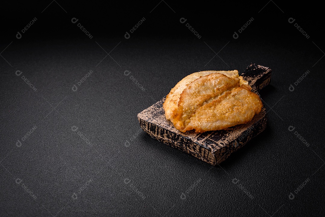 Deliciosas costeletas de peito de frango empanadas com sal, especiarias e ervas sobre um fundo escuro de concreto