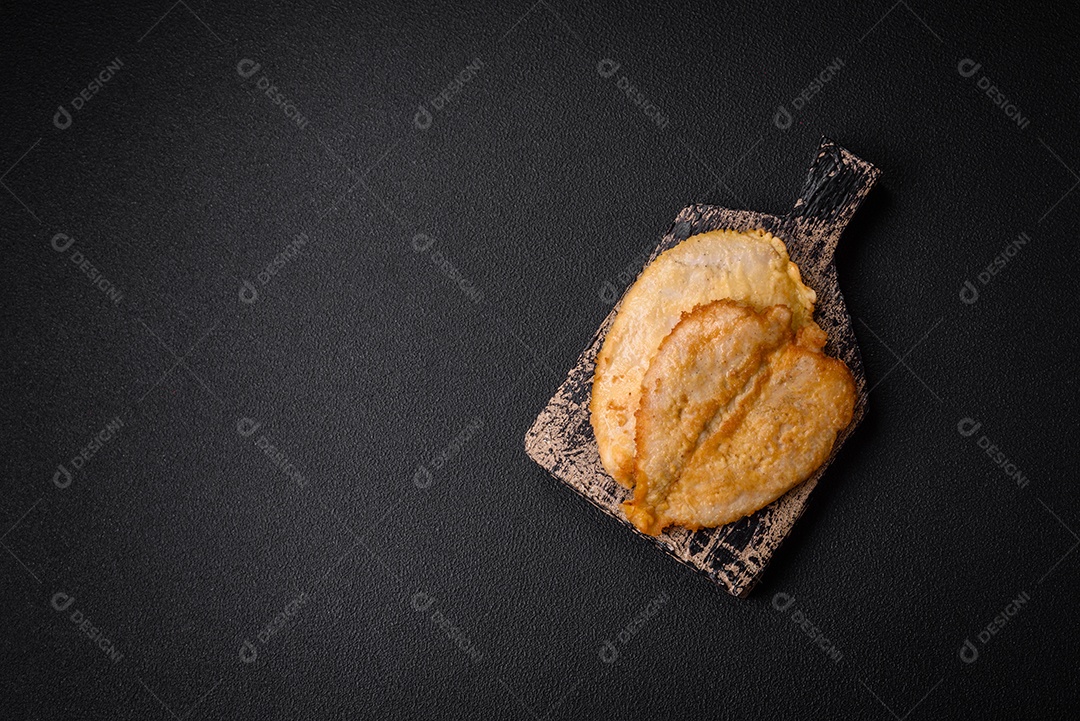 Deliciosas costeletas de peito de frango empanadas com sal, especiarias e ervas sobre um fundo escuro de concreto