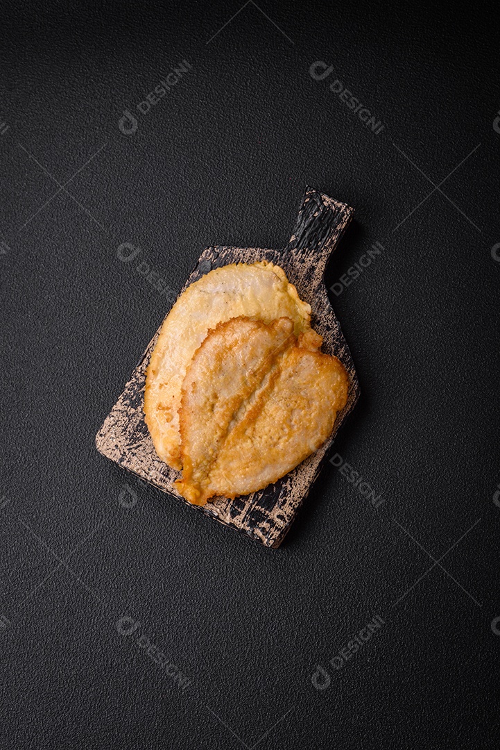 Deliciosas costeletas de peito de frango empanadas com sal, especiarias e ervas sobre um fundo escuro de concreto