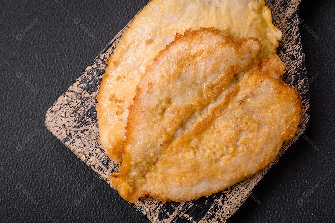 Deliciosas costeletas de peito de frango empanadas com sal, especiarias e ervas sobre um fundo escuro de concret