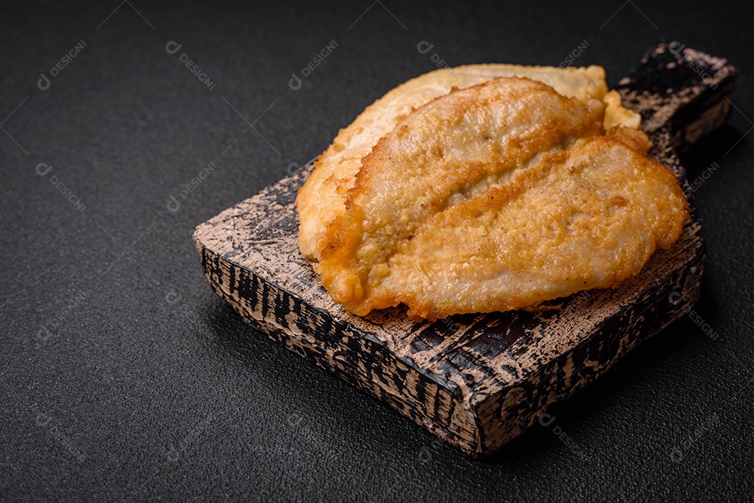 Deliciosas costeletas de peito de frango empanadas com sal, especiarias e ervas sobre um fundo escuro de concreto