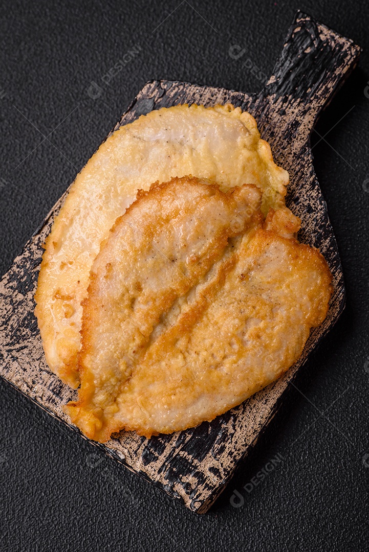 Deliciosas costeletas de peito de frango empanadas com sal, especiarias e ervas sobre um fundo escuro de concreto