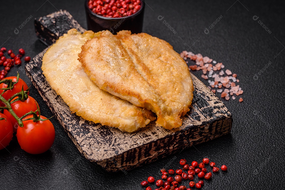 Deliciosas costeletas de peito de frango empanadas com sal, especiarias e ervas sobre um fundo escuro de concreto