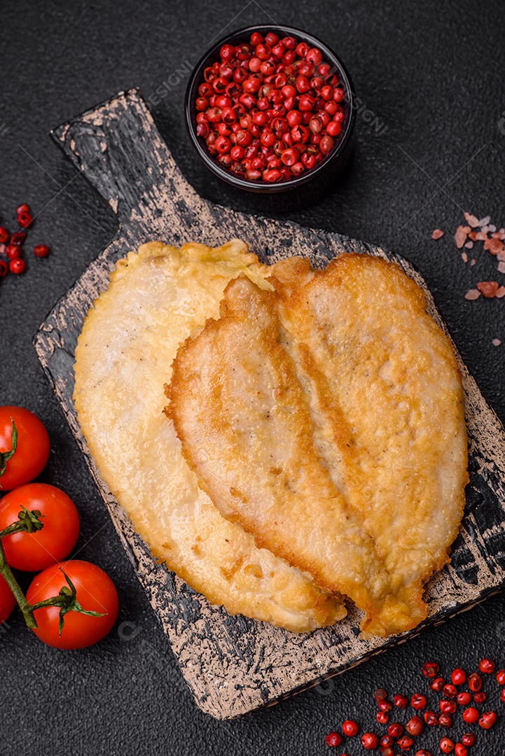 Deliciosas costeletas de peito de frango empanadas com sal, especiarias e ervas sobre um fundo escuro de concreto