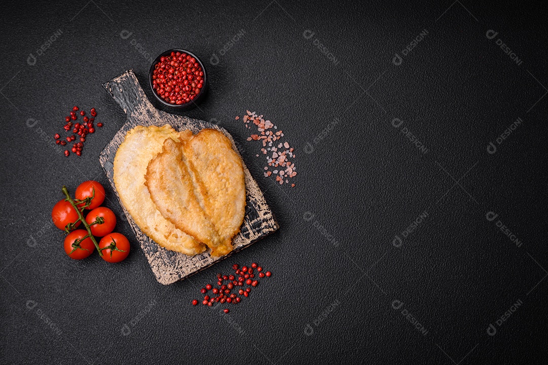 Deliciosas costeletas de peito de frango empanadas com sal, especiarias e ervas sobre um fundo escuro de concreto