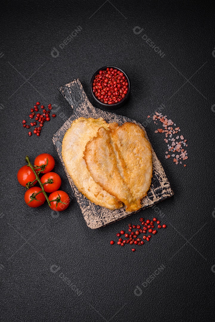 Deliciosas costeletas de peito de frango empanadas com sal, especiarias e ervas sobre um fundo escuro de concreto