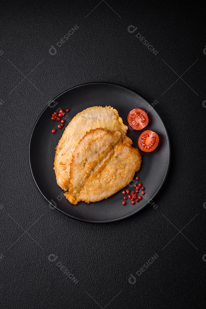 Deliciosas costeletas de peito de frango empanadas com sal, especiarias e ervas sobre um fundo escuro de concreto