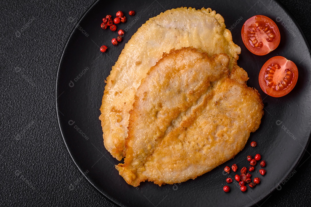 Deliciosas costeletas de peito de frango empanadas com sal, especiarias e ervas sobre um fundo escuro de concreto