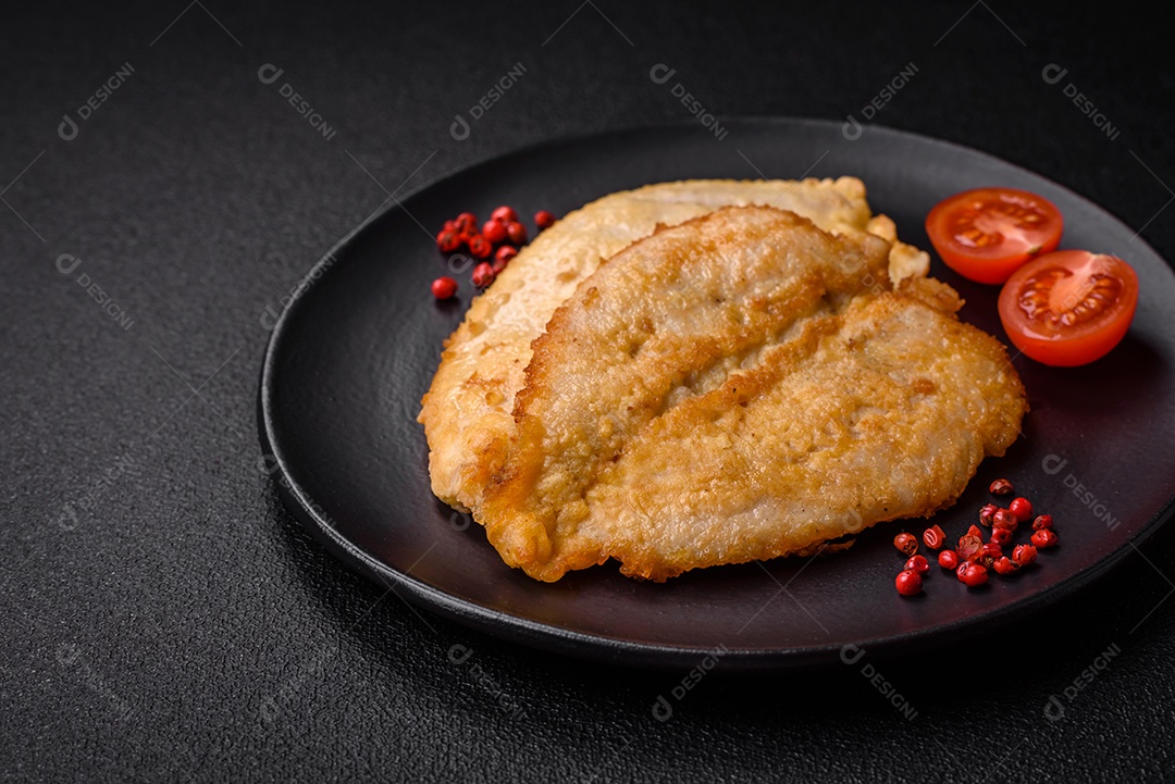 Deliciosas costeletas de peito de frango empanadas com sal, especiarias e ervas sobre um fundo escuro de concreto