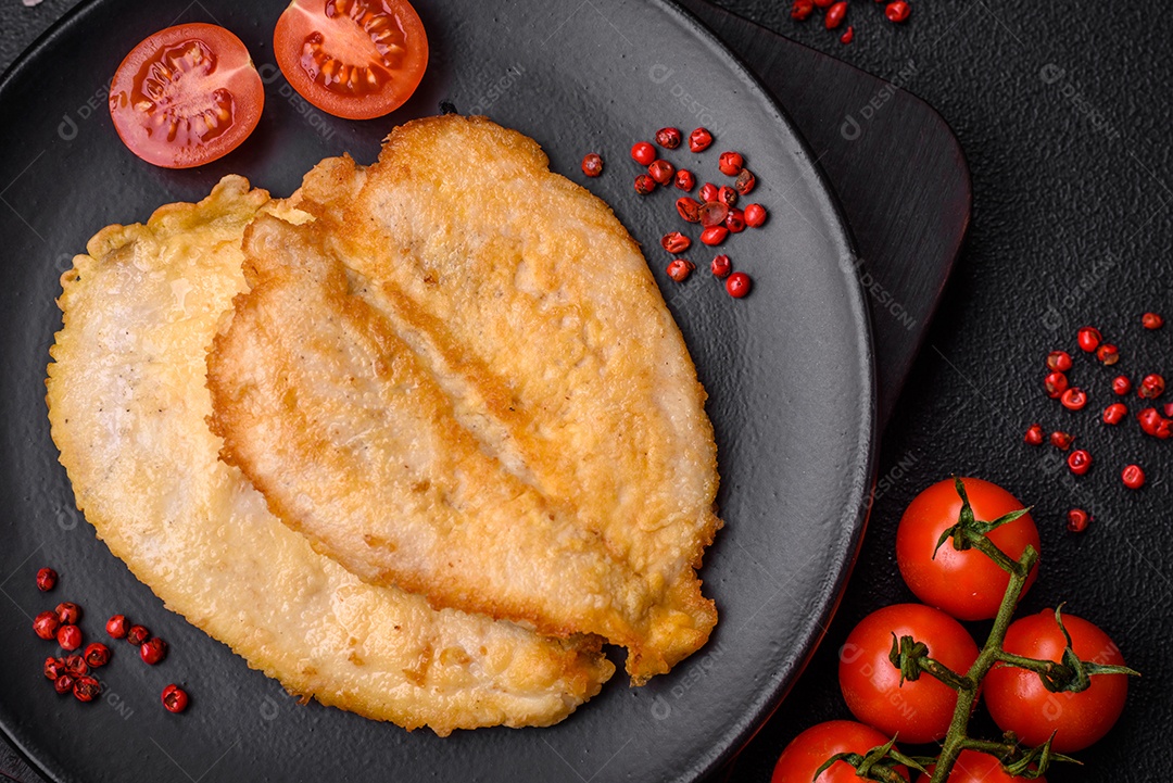 Deliciosas costeletas de peito de frango empanadas com sal, especiarias e ervas sobre um fundo escuro de concreto
