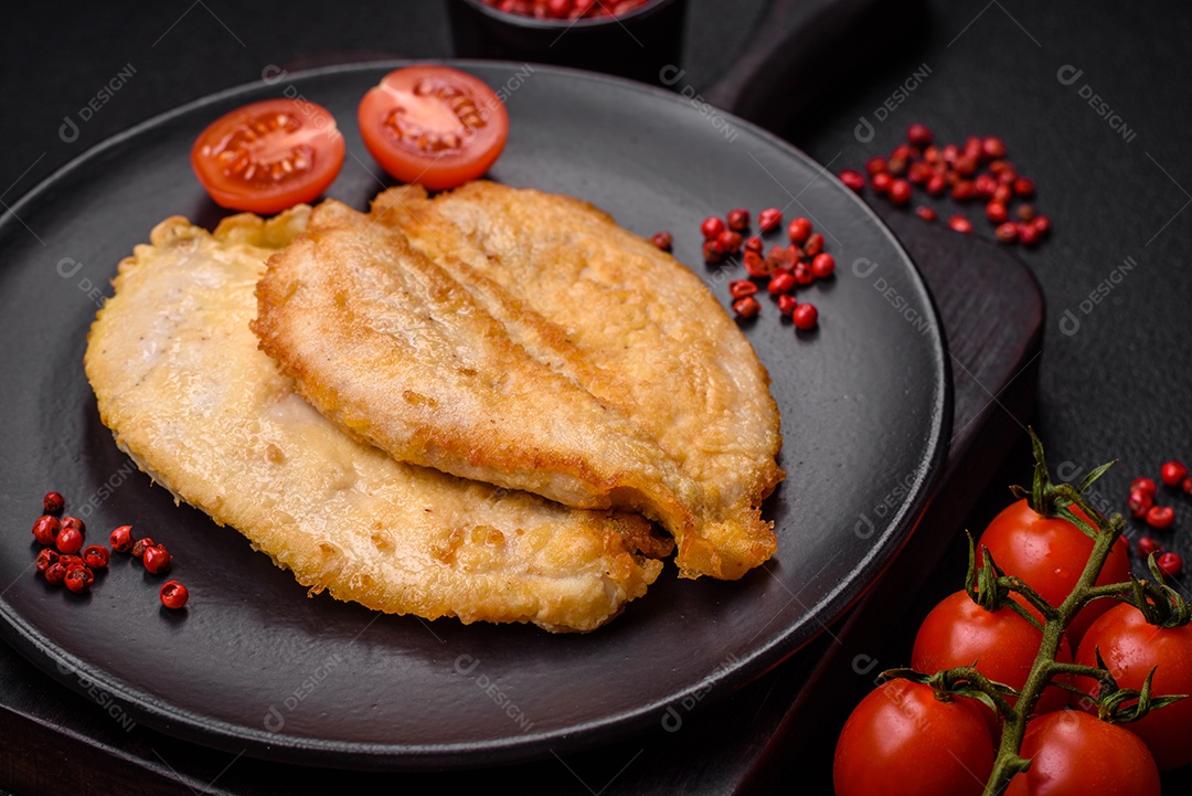 Deliciosas costeletas de peito de frango empanadas com sal, especiarias e ervas sobre um fundo escuro de concreto