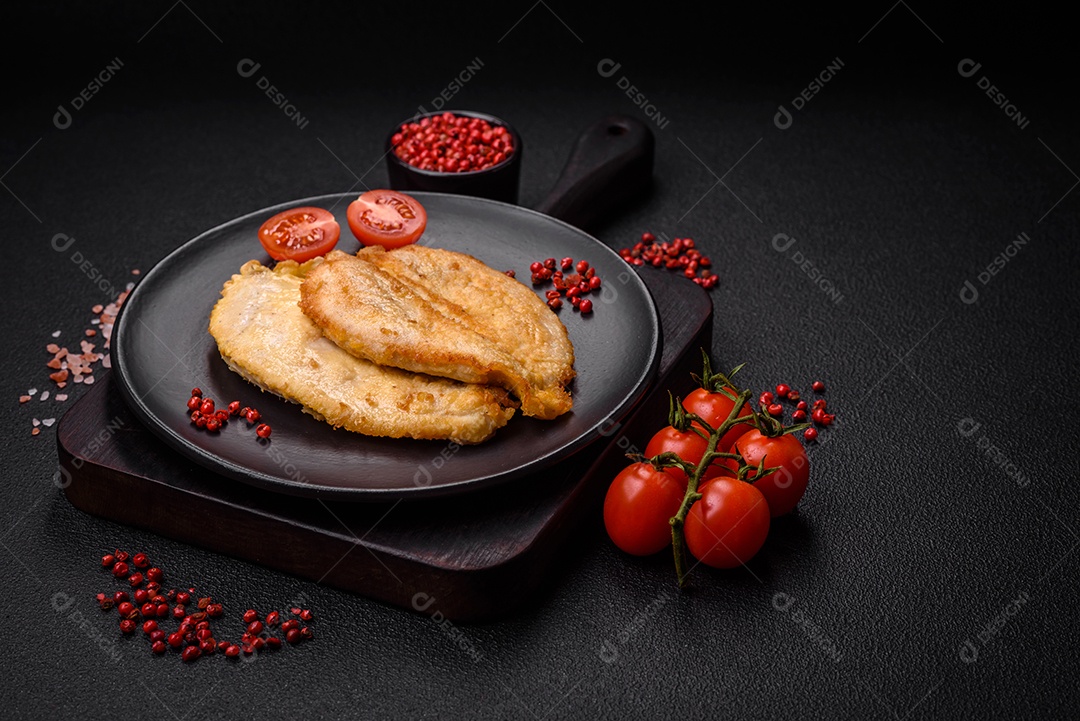 Deliciosas costeletas de peito de frango empanadas com sal, especiarias e ervas sobre um fundo escuro de concreto