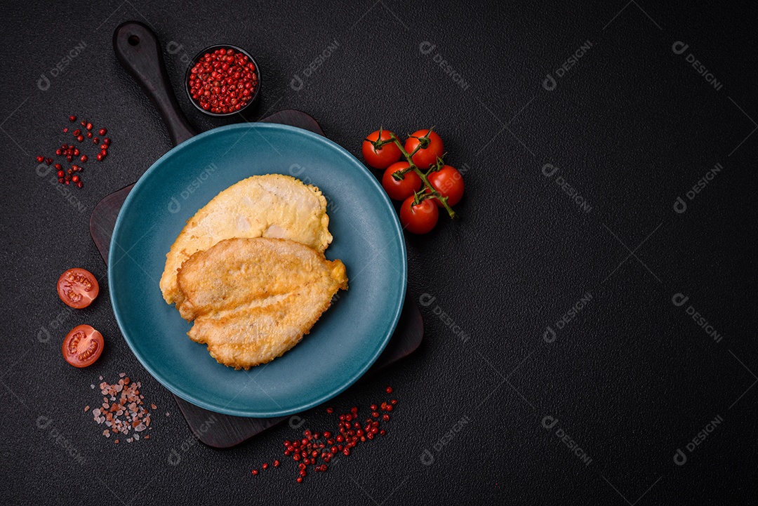 Deliciosas costeletas de peito de frango empanadas com sal, especiarias e ervas sobre um fundo escuro de concreto