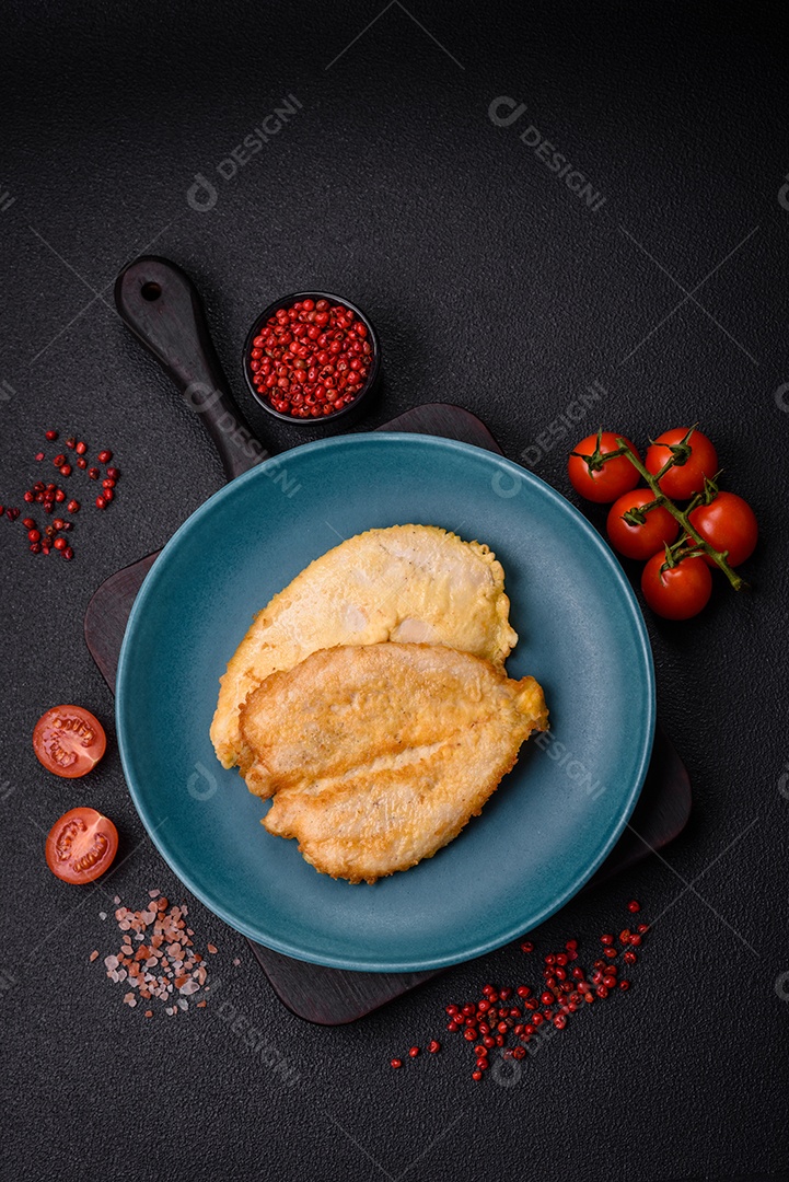 Deliciosas costeletas de peito de frango empanadas com sal, especiarias e ervas sobre um fundo escuro de concreto