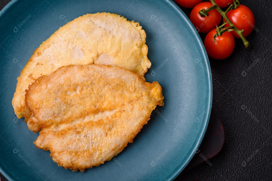 Deliciosas costeletas de peito de frango empanadas com sal, especiarias e ervas sobre um fundo escuro de concreto