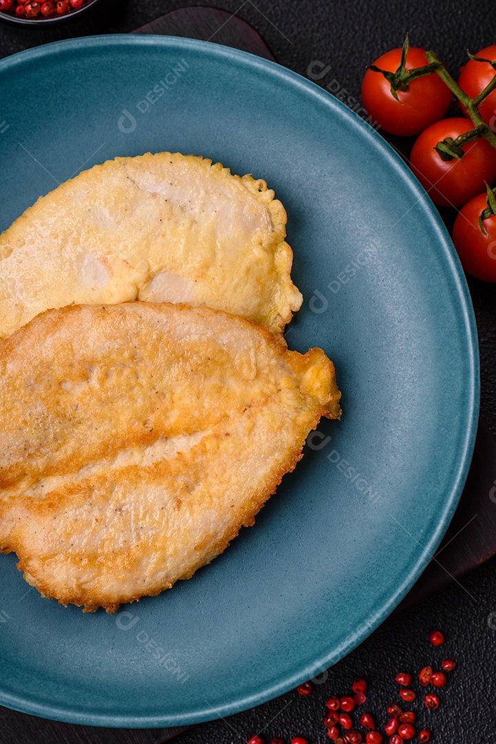 Deliciosas costeletas de peito de frango empanadas com sal, especiarias e ervas sobre um fundo escuro de concreto