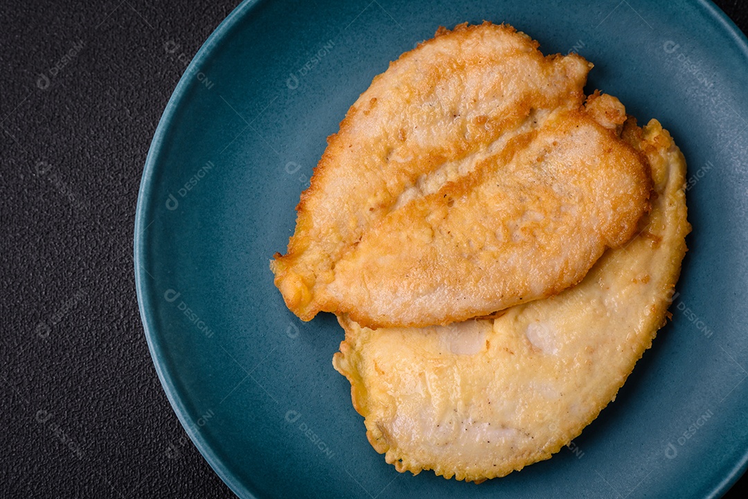 Deliciosas costeletas de peito de frango empanadas com sal, especiarias e ervas sobre um fundo escuro de concreto