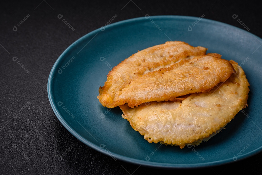 Deliciosas costeletas de peito de frango empanadas com sal, especiarias e ervas sobre um fundo escuro de concreto