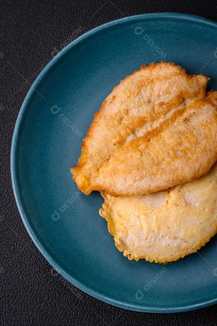 Deliciosas costeletas de peito de frango empanadas com sal, especiarias e ervas sobre um fundo escuro de concreto