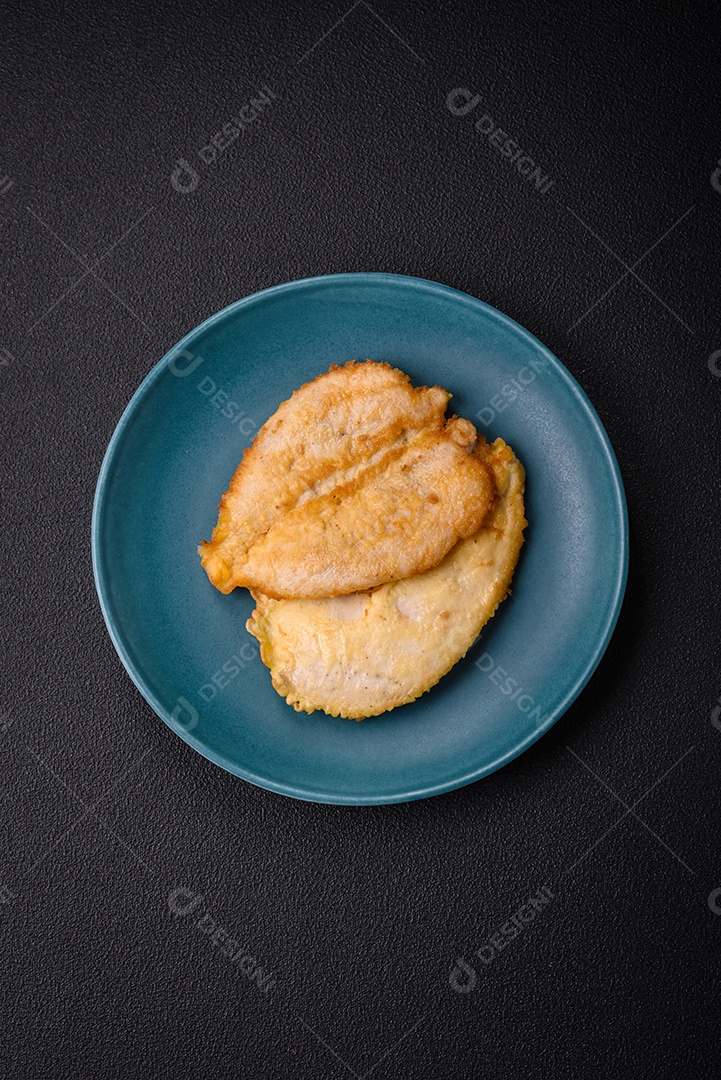 Deliciosas costeletas de peito de frango empanadas com sal, especiarias e ervas sobre um fundo escuro de concreto