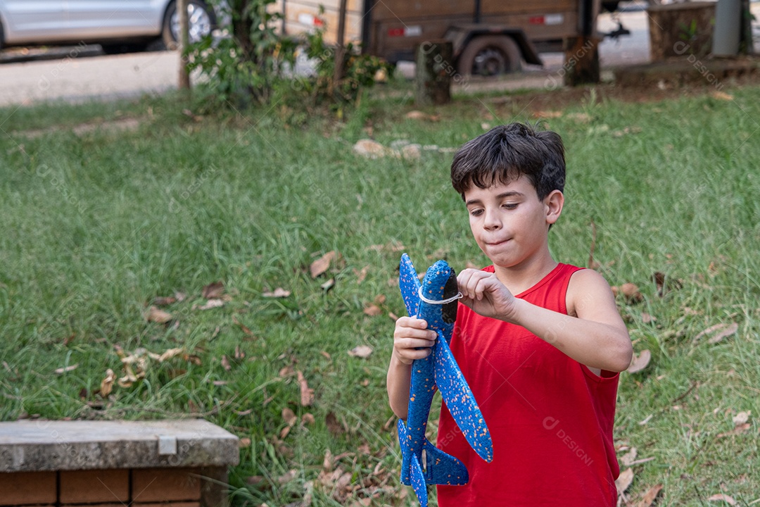 Criança brasileira de 10 anos brincando com seu aviãozinho de isopor em uma tarde ensolarada.