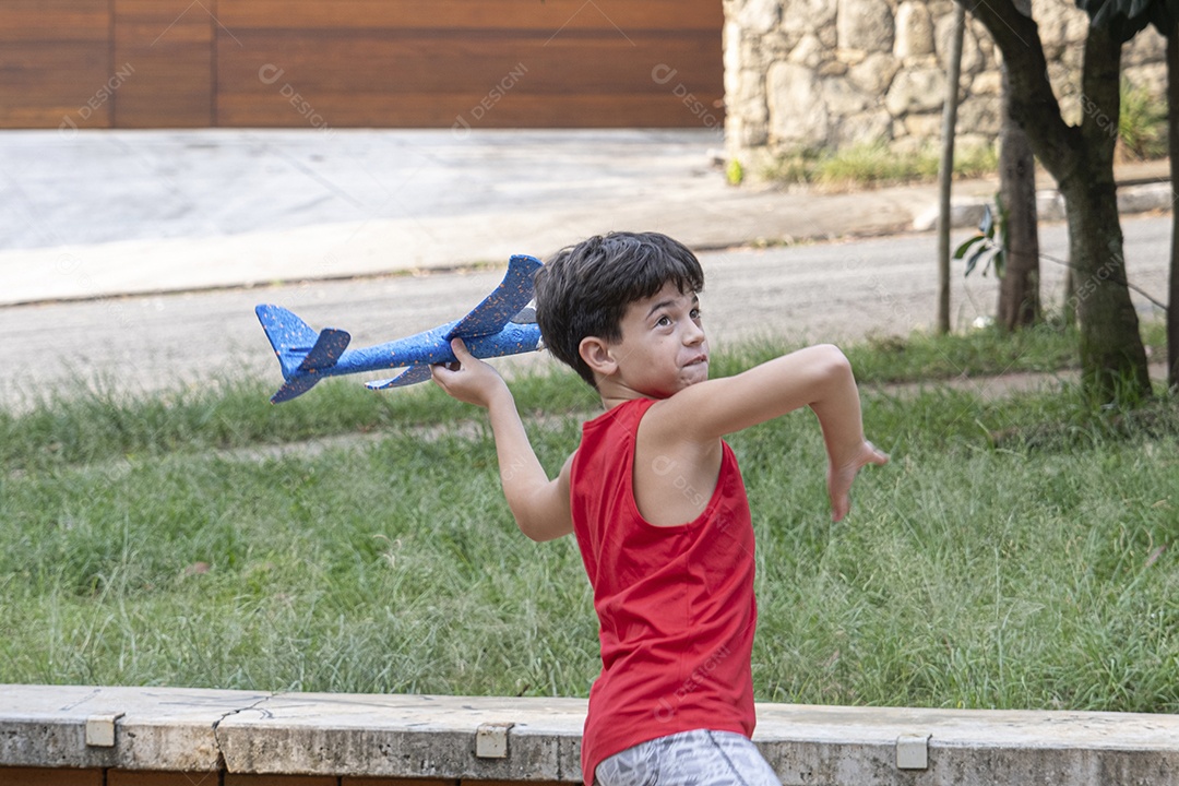 Criança brasileira de 10 anos brincando com seu aviãozinho de isopor em uma tarde ensolarada.