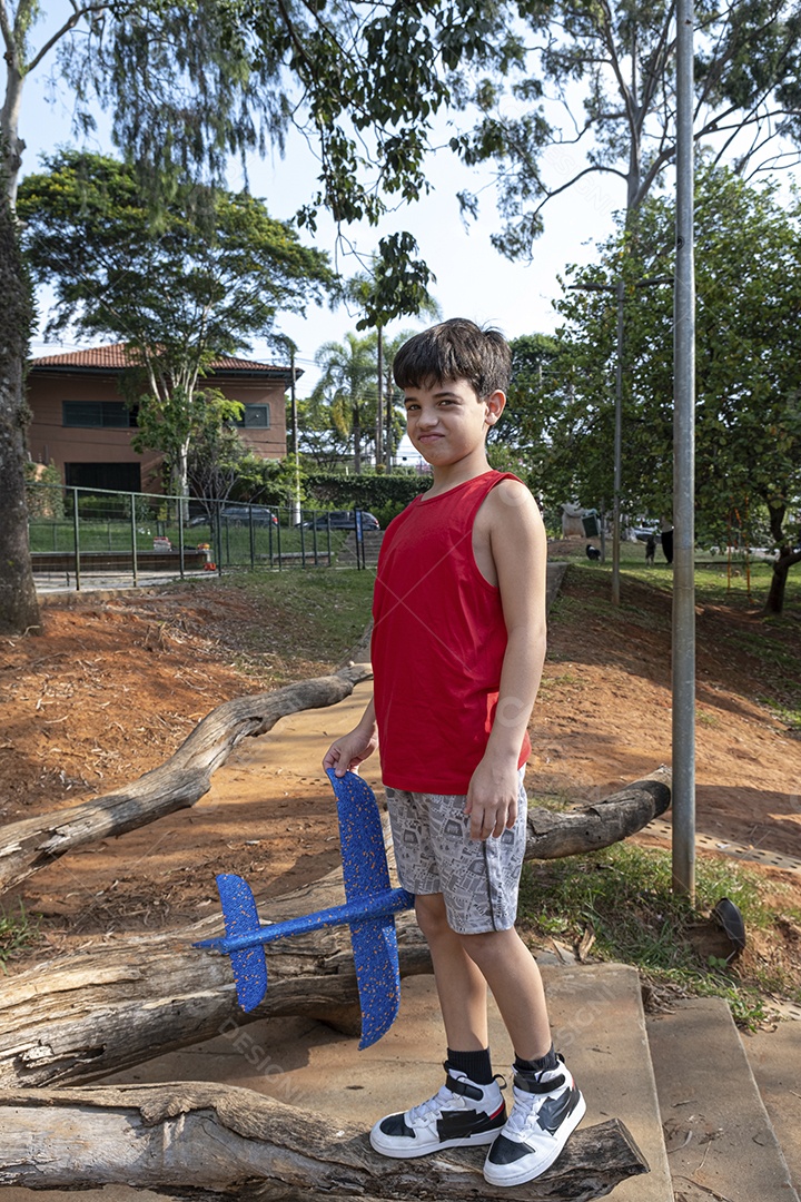 Criança brasileira de 10 anos brincando com seu aviãozinho de isopor em uma tarde ensolarada.