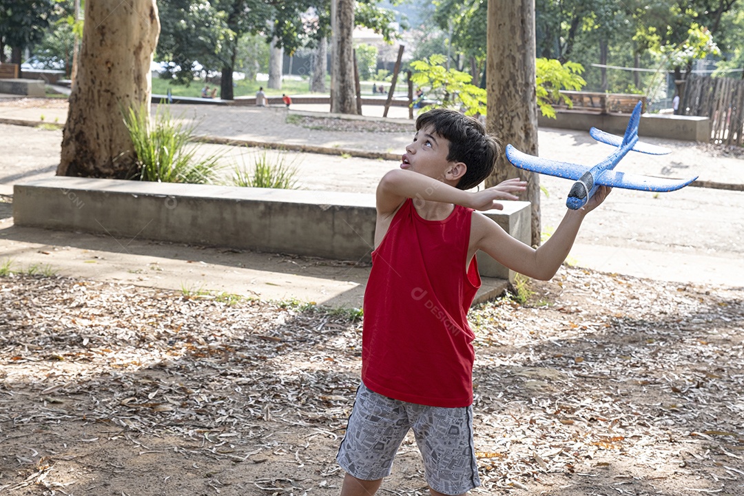 Criança brasileira de 10 anos brincando com seu aviãozinho de isopor em uma tarde ensolarada.