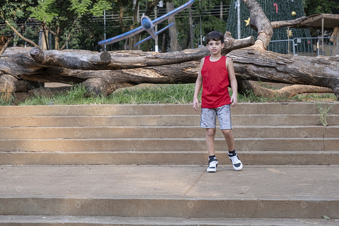 Criança brasileira de 10 anos brincando com seu aviãozinho de isopor em uma tarde ensolarada.