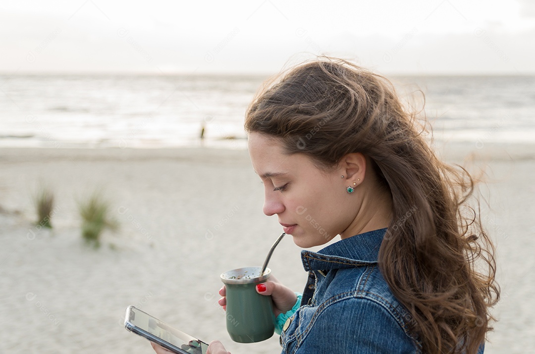 Mulher jovem e bonita bebendo Chimarao, mate (bebida de infusão de erva-mate) na praia do Uruguai.