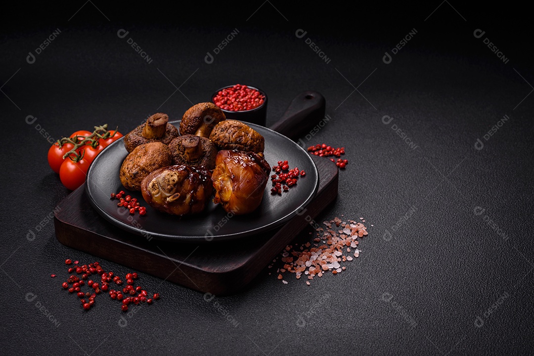 Deliciosos champignon inteiros e suculentos assados ​​na grelha com sal e especiarias em uma placa de cerâmica sobre um fundo escuro de concreto