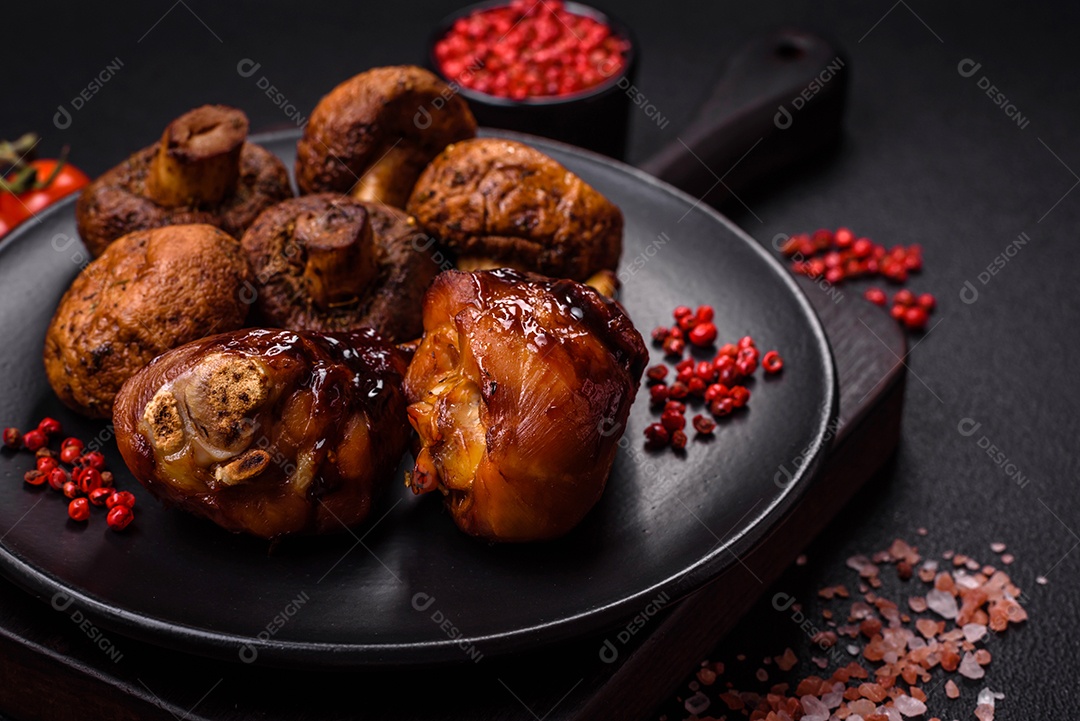Deliciosos champignon inteiros e suculentos assados ​​na grelha com sal e especiarias em uma placa de cerâmica sobre um fundo escuro de concreto