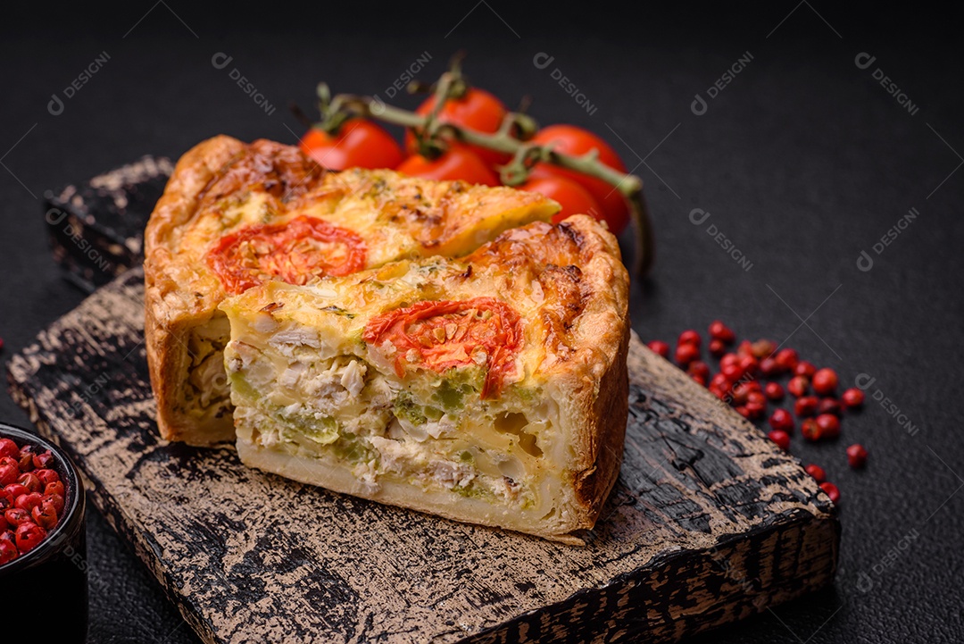 Deliciosa quiche com tomate, queijo, frango, especiarias e ervas sobre um fundo escuro de concreto