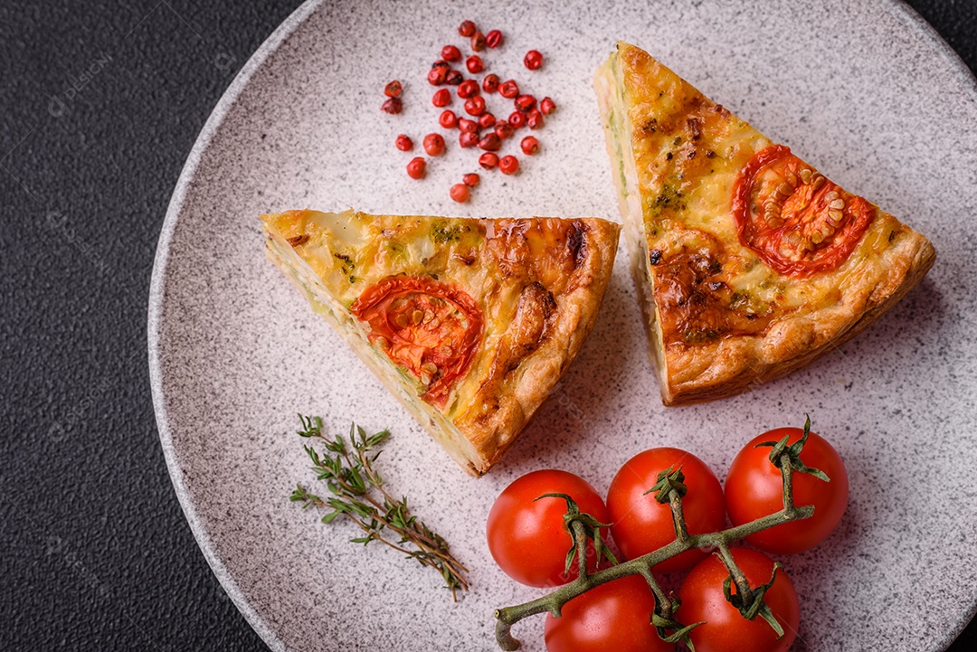 Deliciosa quiche com tomate, queijo, frango, especiarias e ervas sobre um fundo escuro de concreto