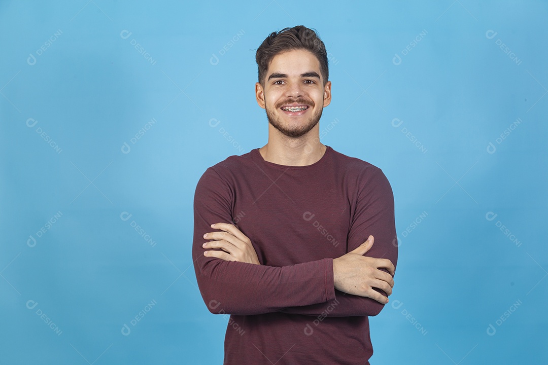 Homem sorridente de braços cruzados sobre fundo isolado azul.