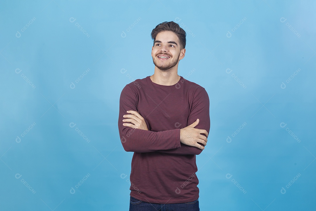 Homem sorridente de braços cruzados sobre um fundo isolado azul.