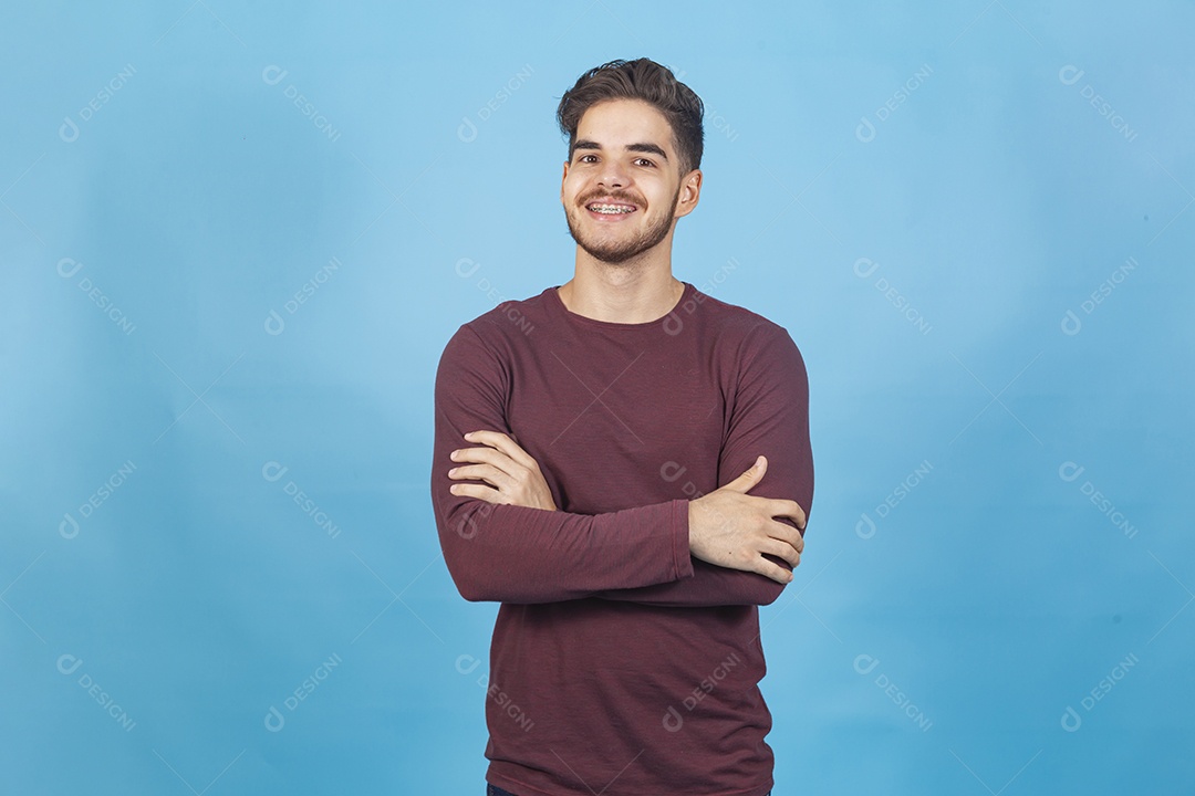 Homem sorridente de braços cruzados sobre um fundo isolado azul.