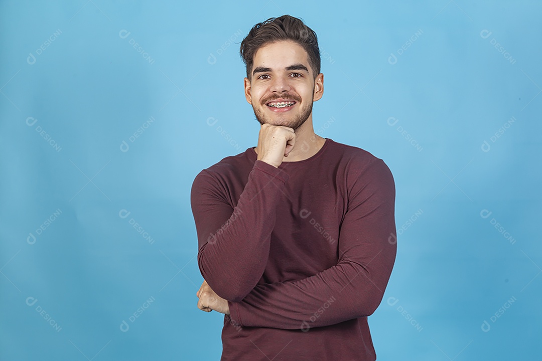 Homem sorridente com mão no queixo sobre fundo isolado azul.
