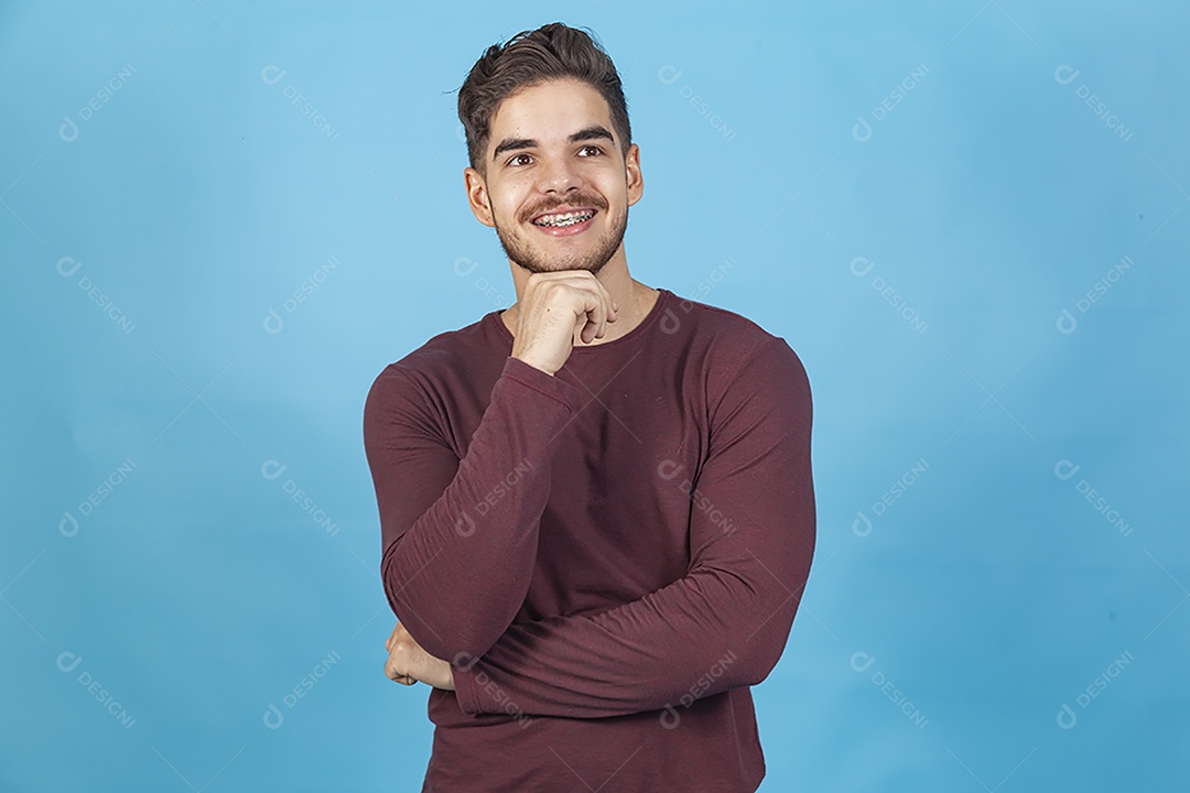 Homem sorridente com mão no queixo sobre fundo isolado azul.