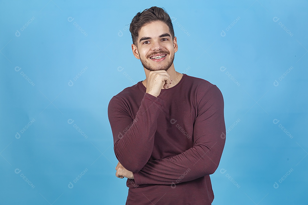 Homem sorridente com mão no queixo sobre fundo isolado azul.