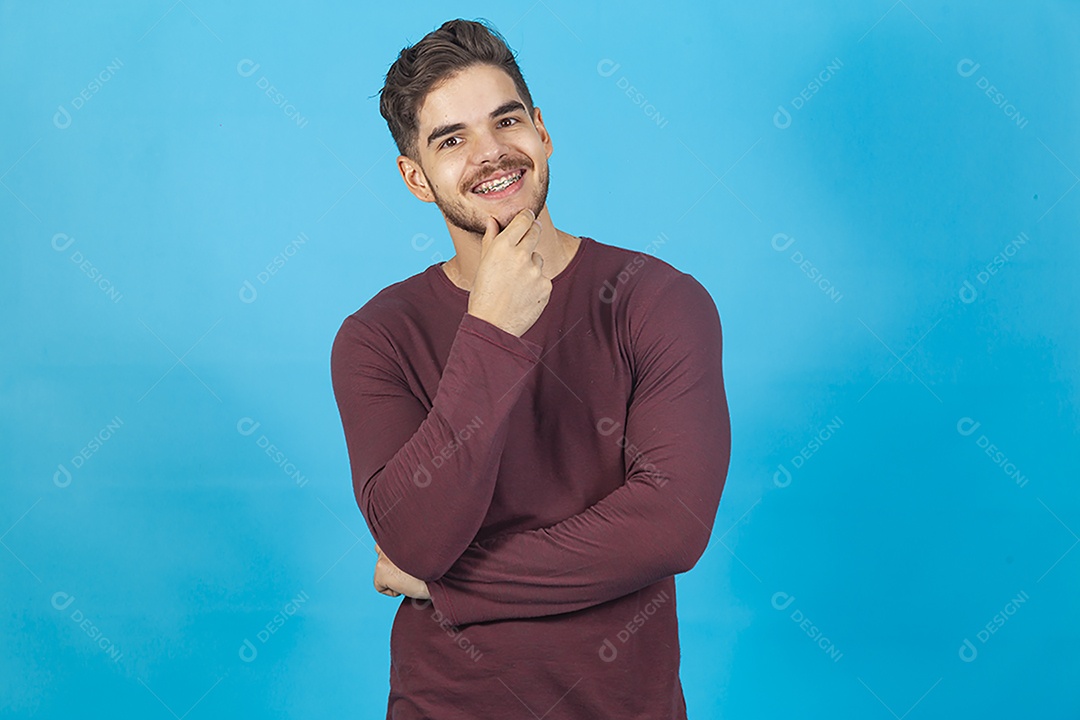 Homem sorridente de camisa manga longa sobre fundo isolado azul.