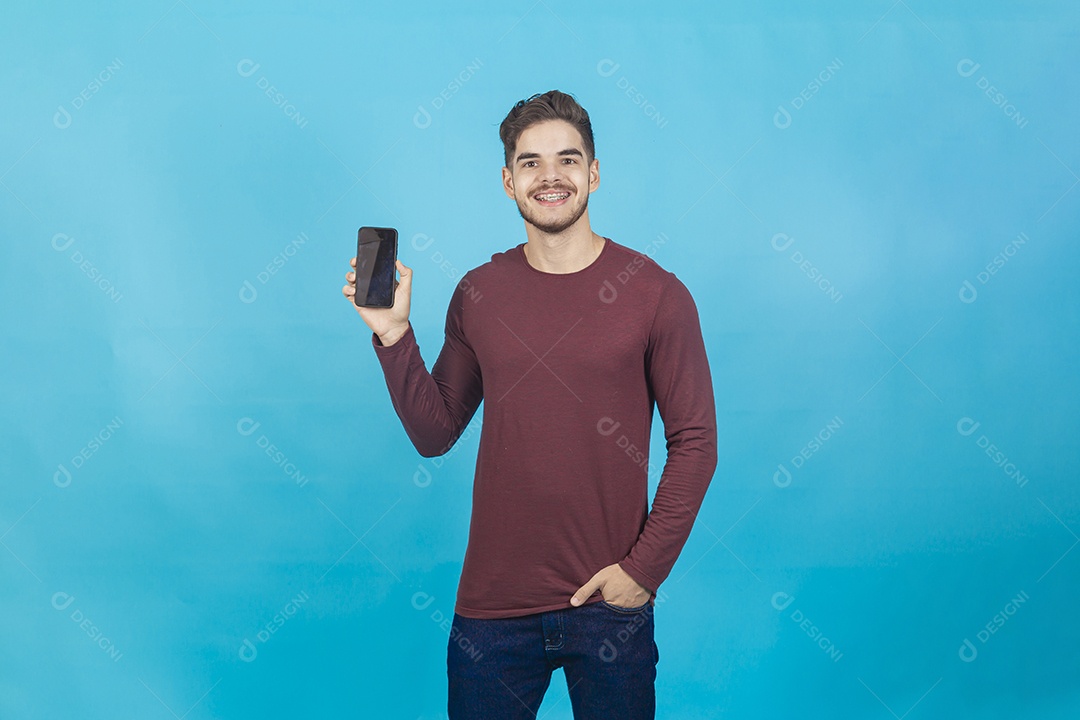 Homem sorridente segurando celular sobre um fundo isolado azul.