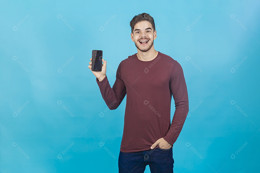 Homem sorridente segurando celular sobre um fundo isolado azul.