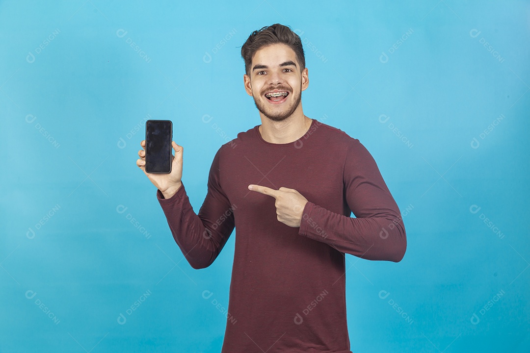 Homem sorridente segurando celular sobre um fundo isolado azul.