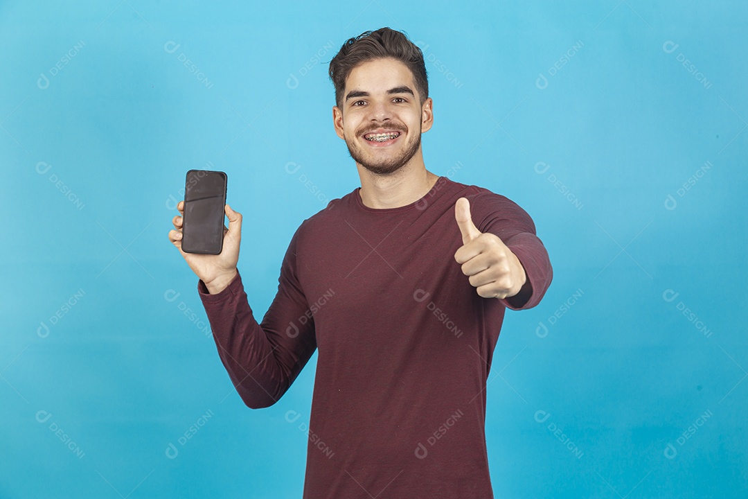 Homem sorridente segurando celular sobre um fundo isolado azul.