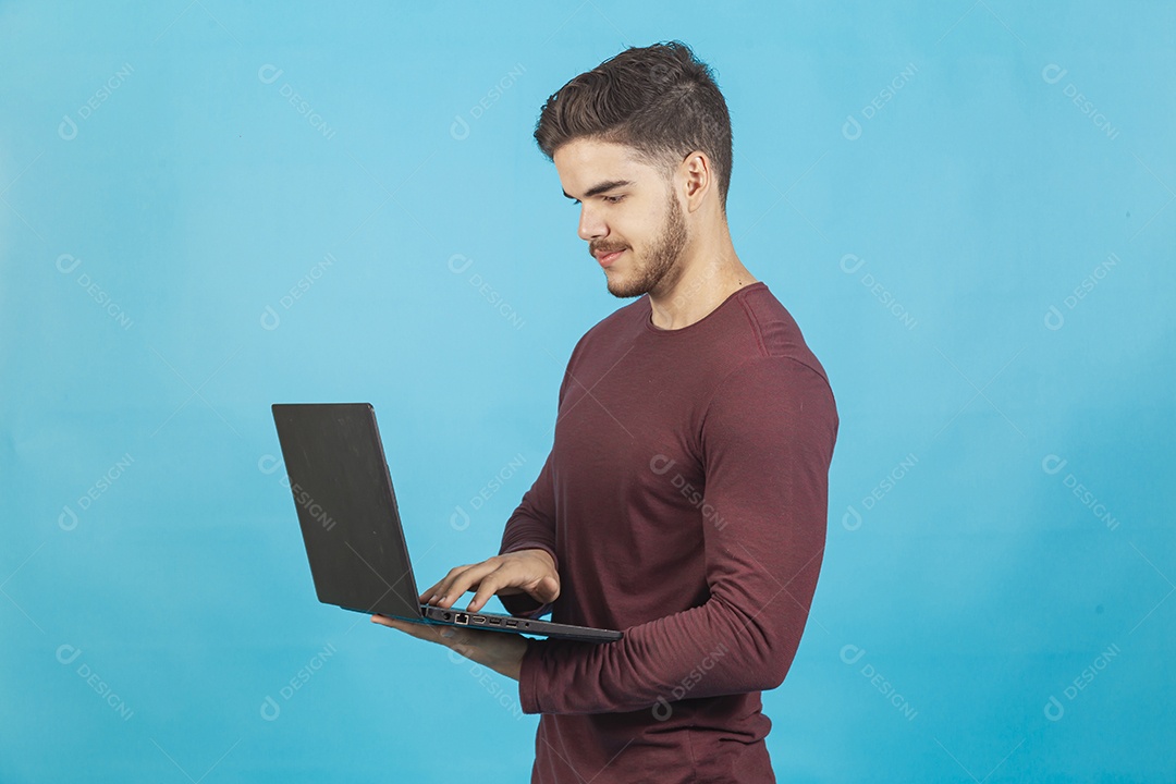 Homem jovem segurando notebook sobre fundo isolado azul.