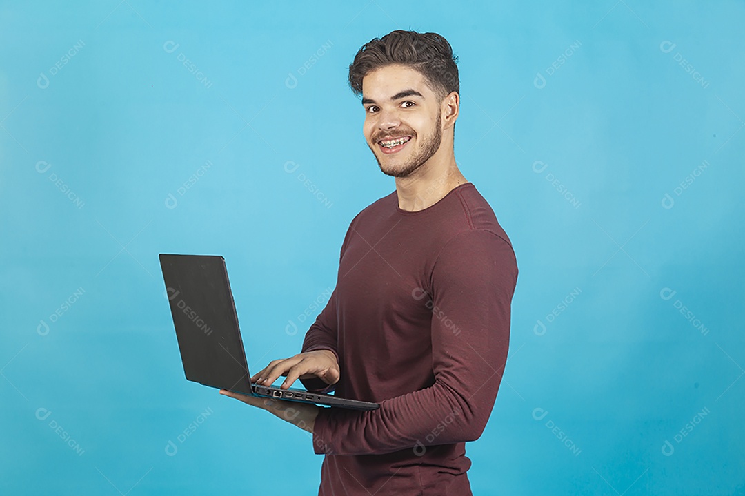 Homem sorridente segurando notebook sobre fundo isolado azul.