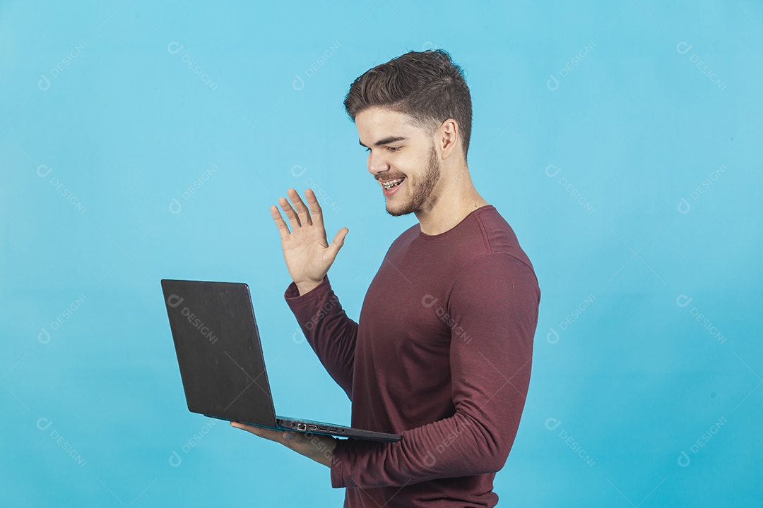 Homem jovem segurando notebook sobre fundo isolado azul.